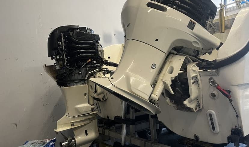 Two white outboard motors with covers removed, mounted on a boat transom in a workshop.
